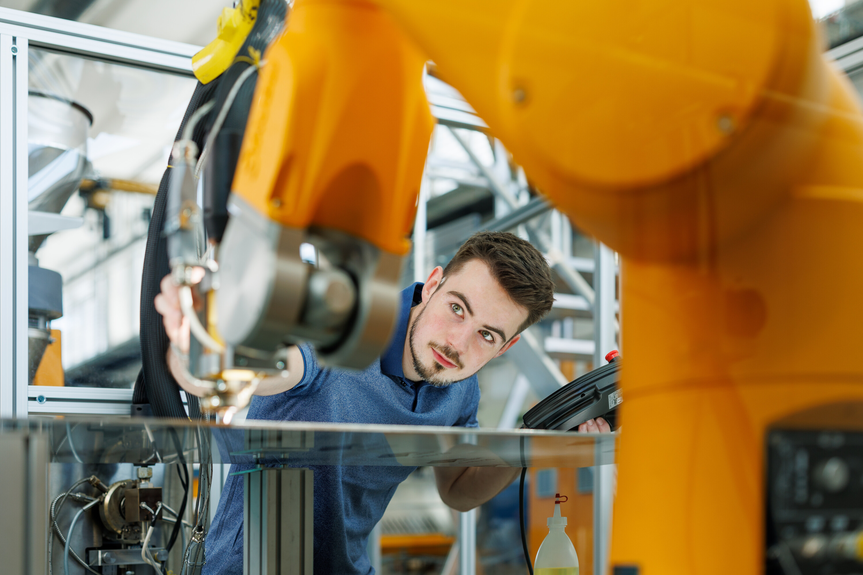 Junger Mann schaut zwischen Industrieroboter hindurch (Symbolbild für MSE Ingenieurstudium)