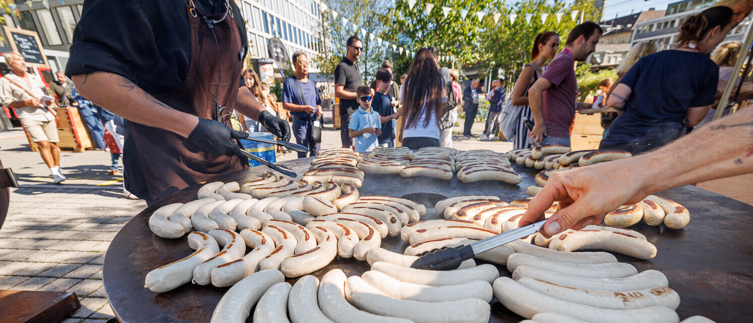 Bratwürste werden im Aussenbereich des Campus St.Gallen auf einer grossen Grillplatte zubereitet.