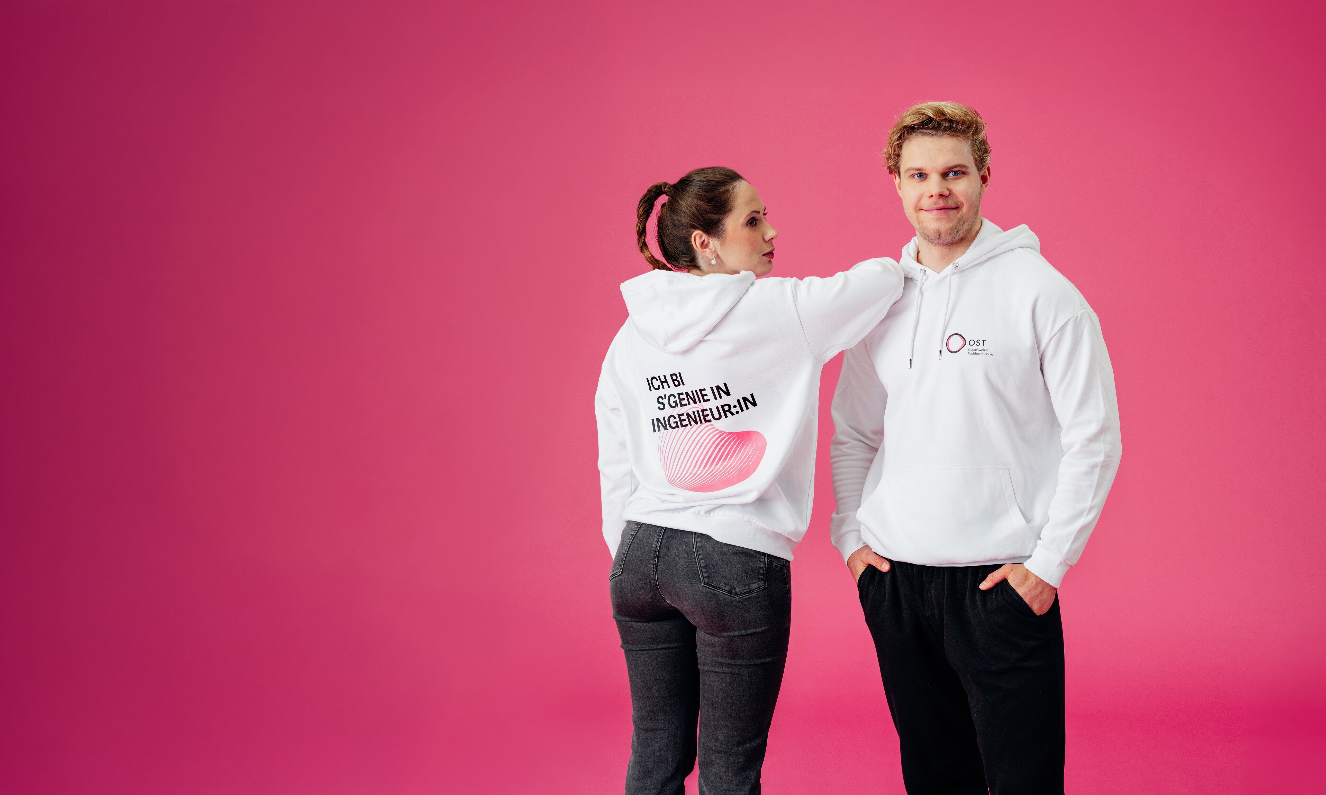 Eine junge Frau und ein Mann in weissen Hoodies vor einem pinkfarbenen Hintergrundd