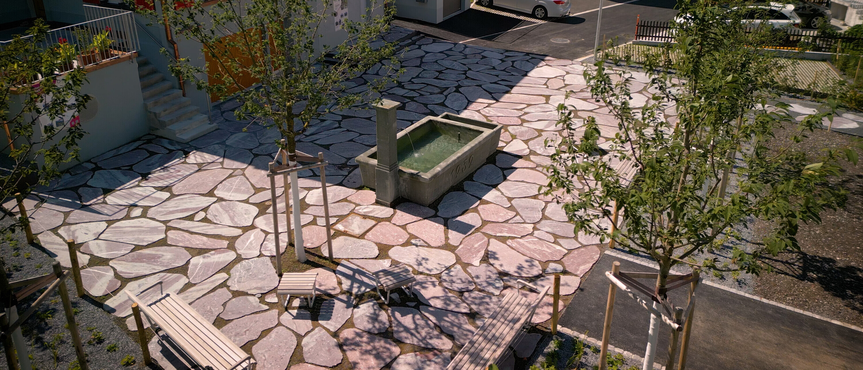 Neugestalteter Platz mit Brunnen, Sitzbänken, Bäumen und Bodenplatten im Quartier Plattenau.