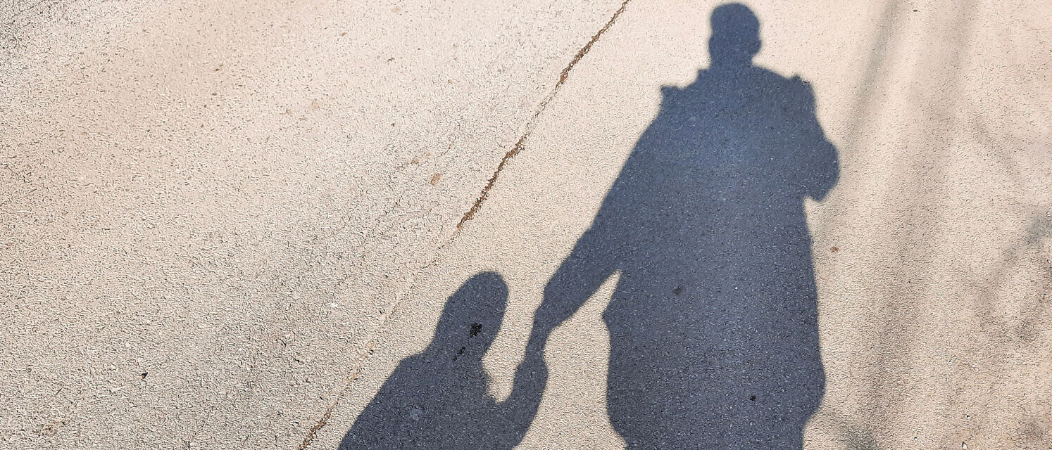 Im Schattenbild hält ein Kind die Hand einer erwachsenen Person.