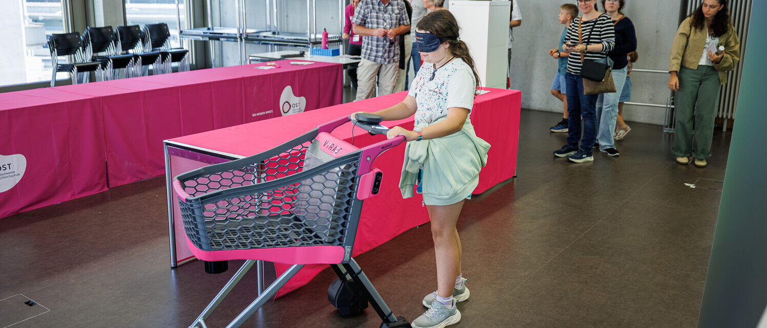 Eine junge Besucherin testet mit verbundenen Augen den intelligenten Einkaufswagen VIRAS.