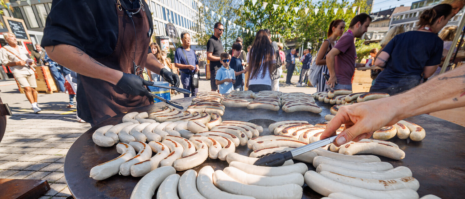 Bratwürste werden im Aussenbereich des Campus St.Gallen auf einer grossen Grillplatte zubereitet.