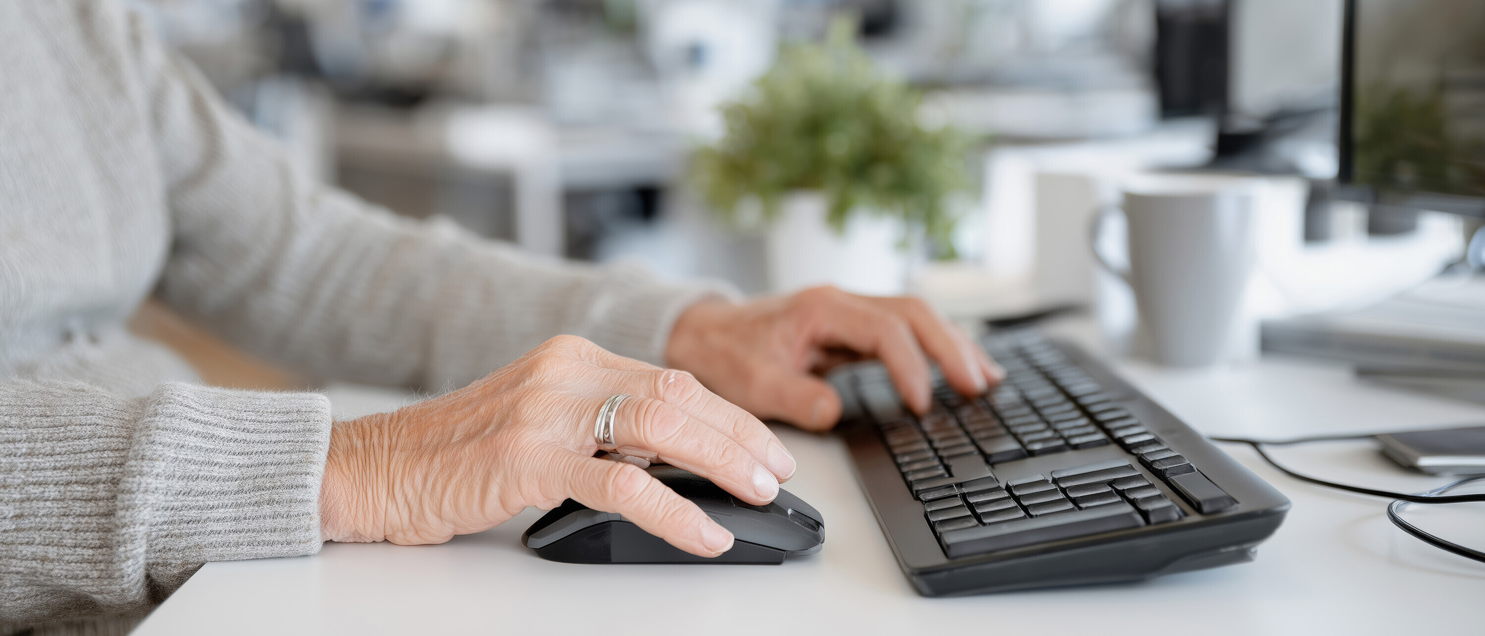Old pensioner man sitting at table and working on computer, concept of socialization and employment of old people Symbolbild: Hände einer älteren Person am Computer am Arbeiten.