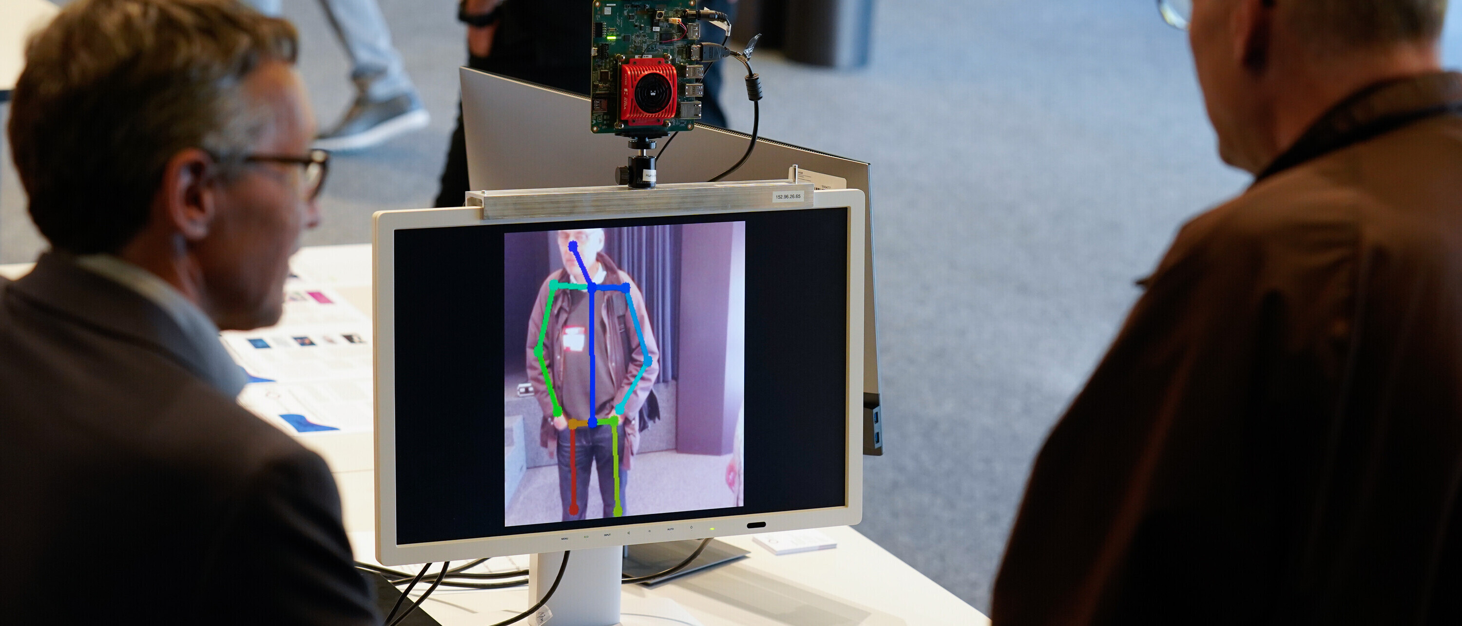 Zwei Männer stehen vor einem Gerät, das mit Künstlicher Intelligenz Menschen identifiziert.