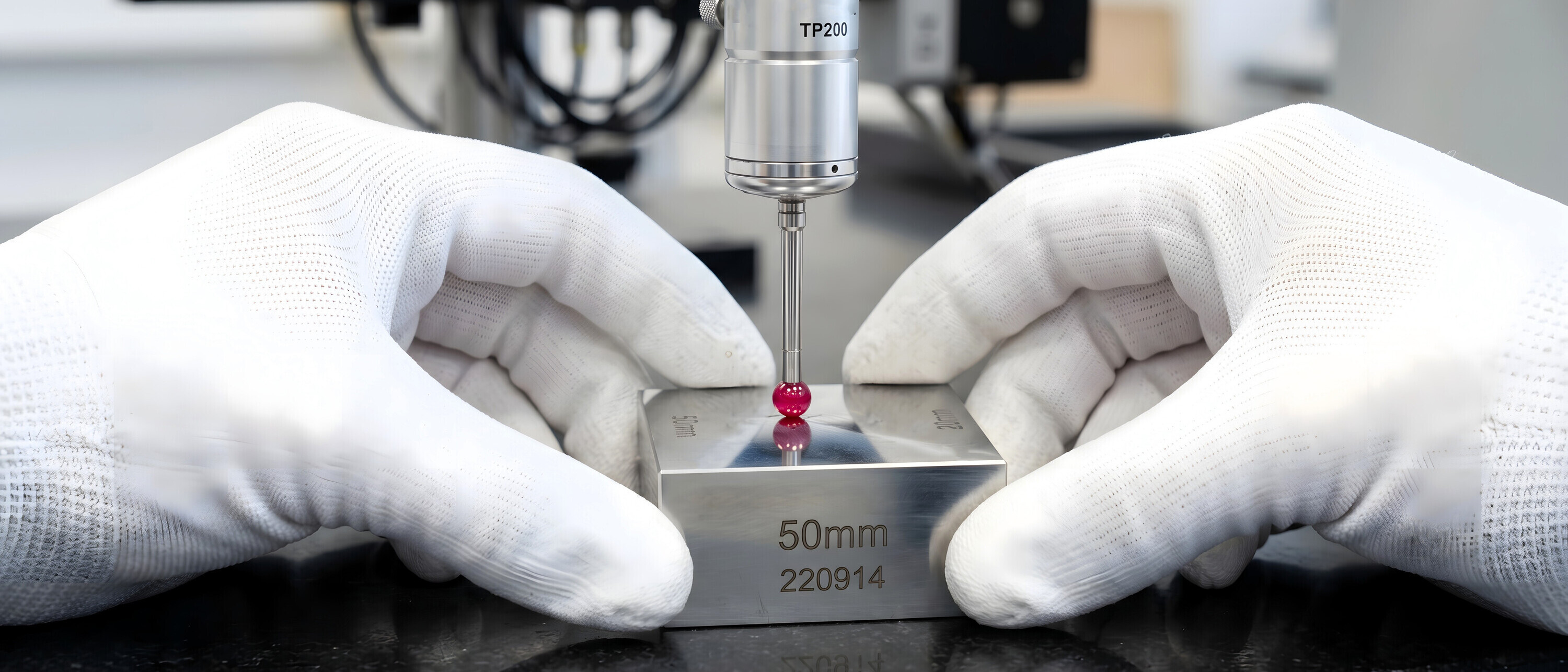 A technician wearing white cotton gloves measuring a steel gauge block with a touch probe sensor