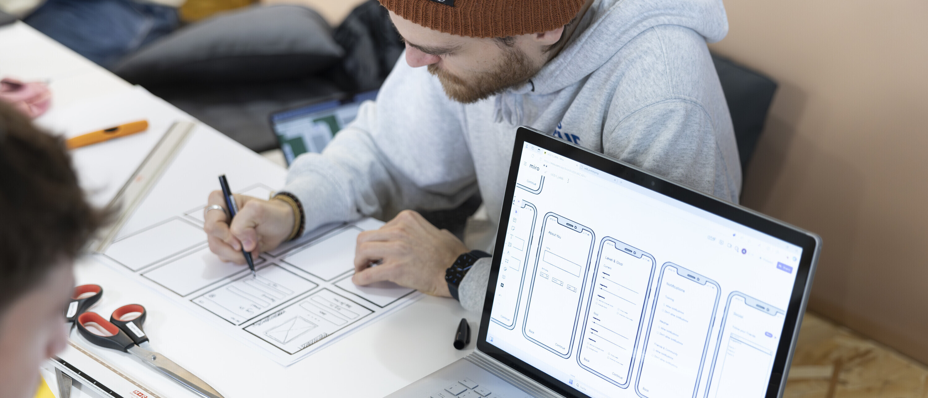 Ein Studierender des Bachelors Digital Design neben einem Laptop mit einem Wireframe