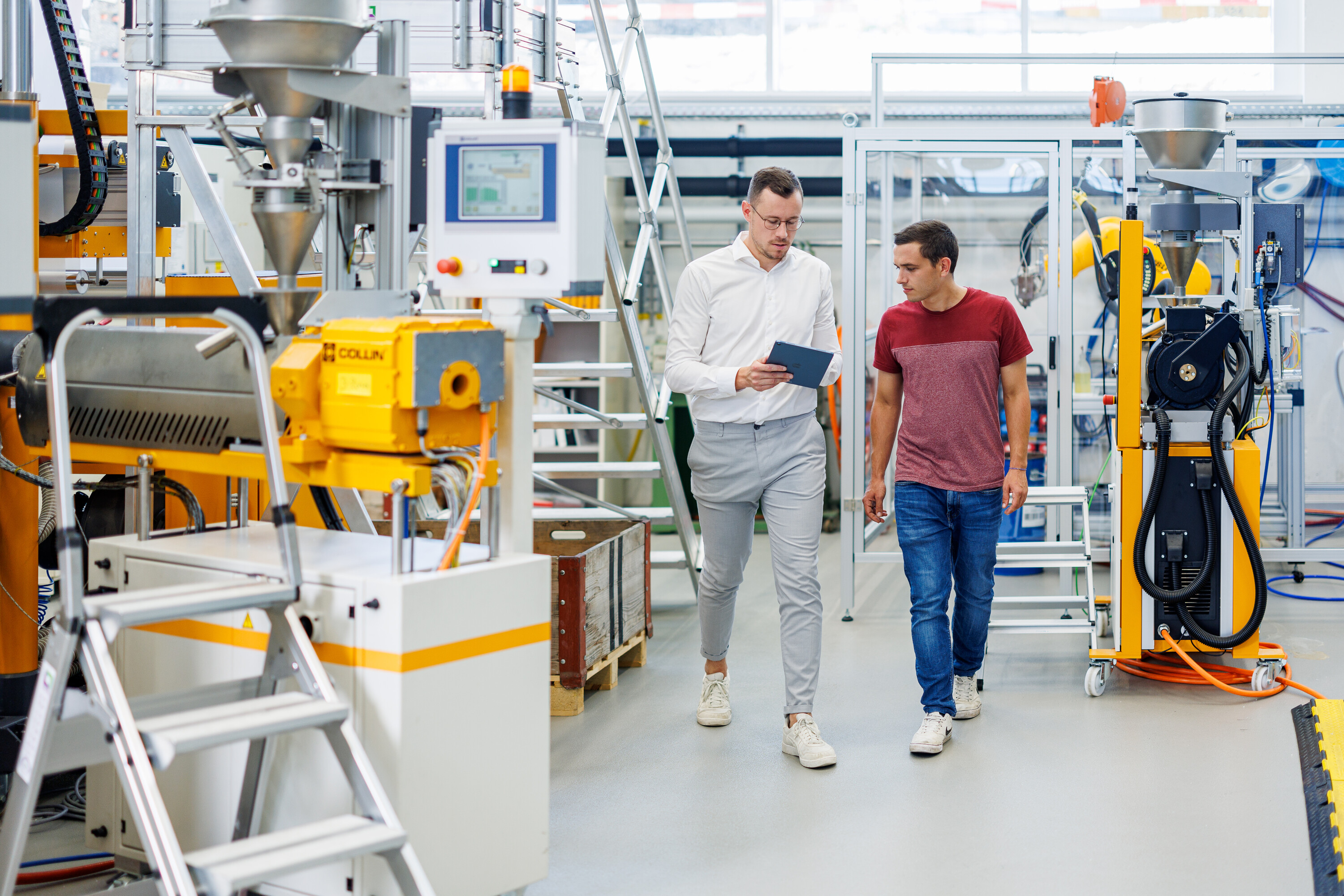 Zwei Studenten des Masters in Business Engineering diskutieren in einer Produktionshalle mit Industrieroboternge