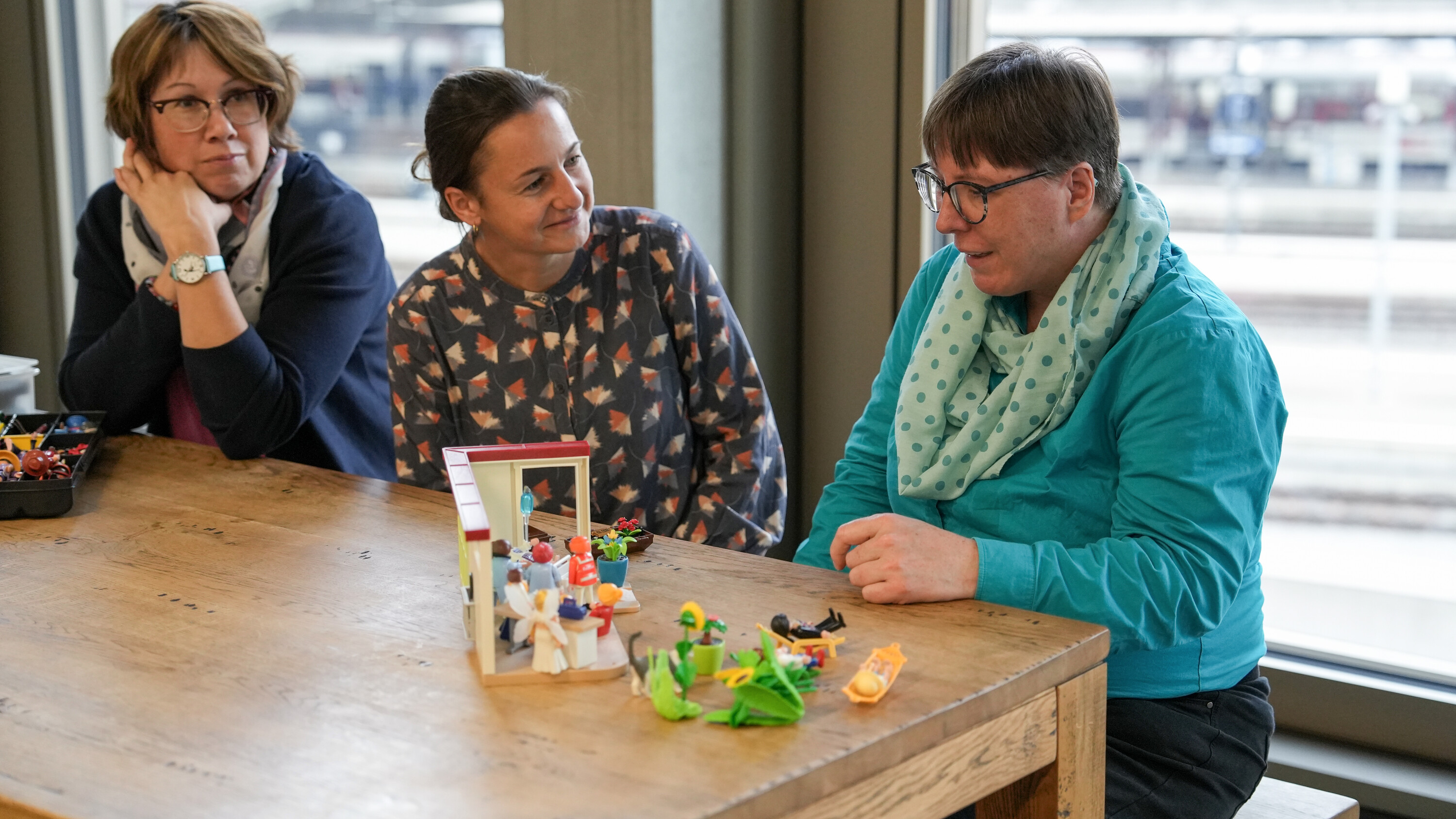 Drei Frauen bauen mit Playmobil eine Palliative Care-Situation nach.